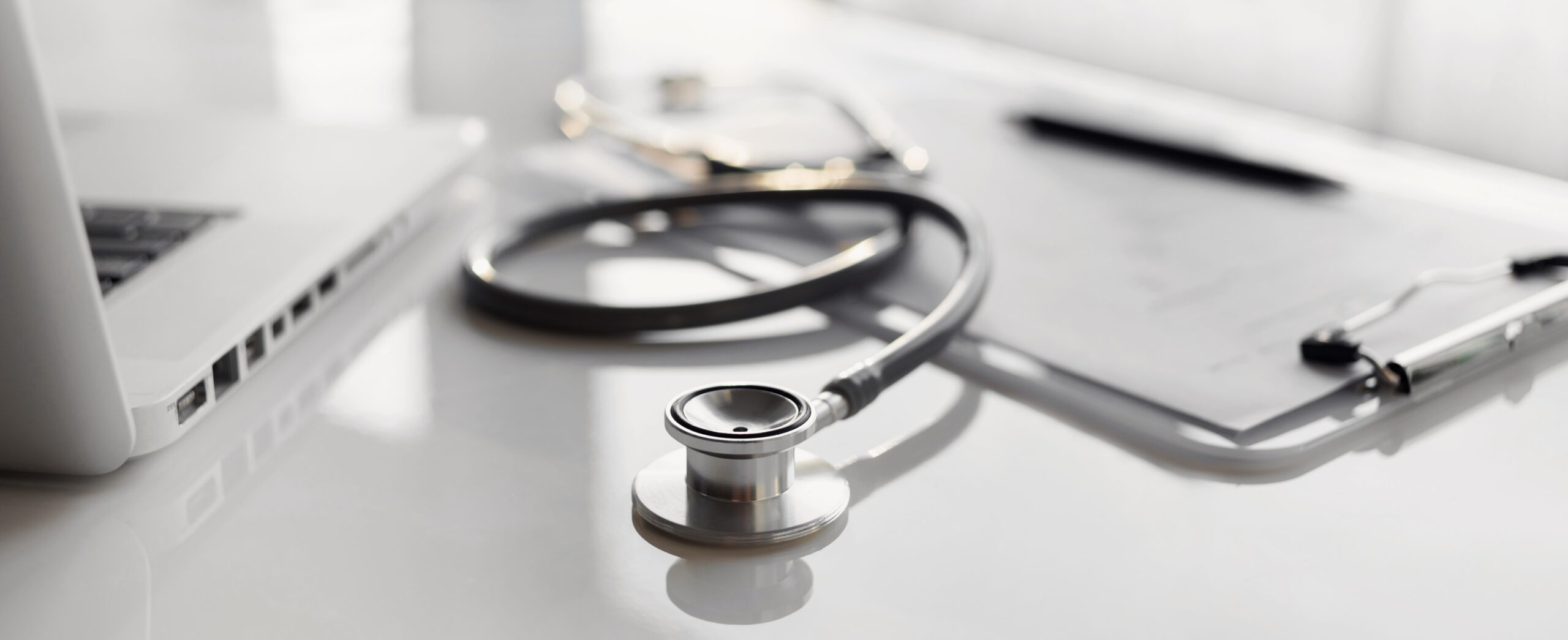 A stethoscope, clipboard, and laptop on a desk